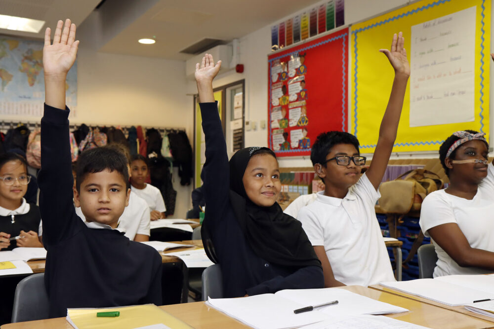 Eager hands up from a group of children to answer a question from the teacher