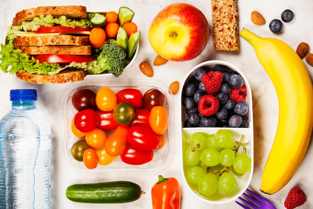 Healthy lunch box with sandwich and fresh vegetables, bottle of water and fruits on wooden background. Top view