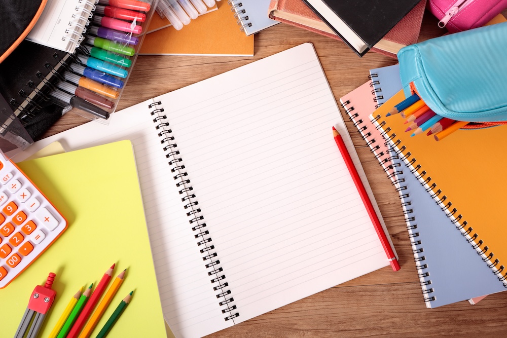 Busy student's desk with open notebook, school bag, text books and various pencils and crayons.