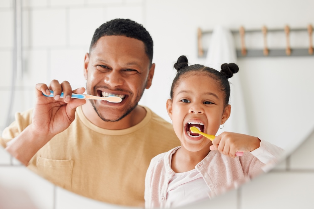 Child, father and brushing teeth in a family home bathroom for dental health and wellness in a mirror. Face of african man and girl kid learning to clean mouth with a toothbrush for oral hygiene.